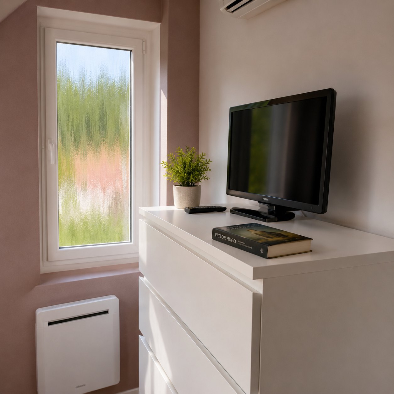 Commode blanche avec télévision dans la seconde chambre, climatiseur au-dessus et radiateur sous la fenêtre